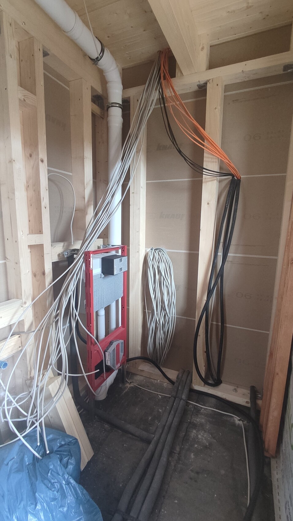 Rohbau-Innenraum: roter Rahmen für Wandtoilette, zahlreiche Rohre und Kabel.