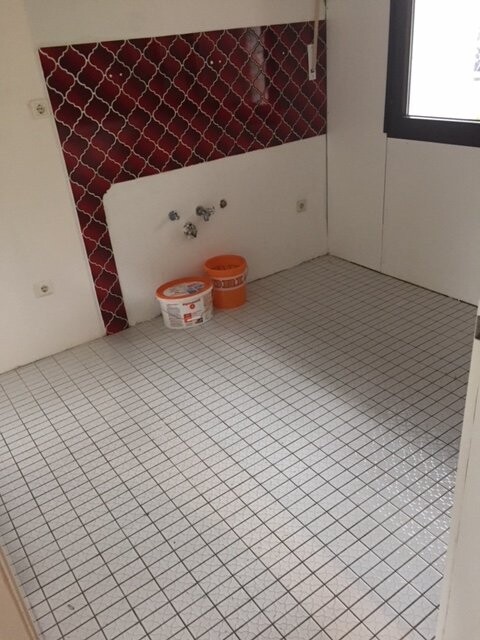 Badezimmer im Bau mit Bodenfliesen, roter Wandfliese und Sanitäranschlüssen