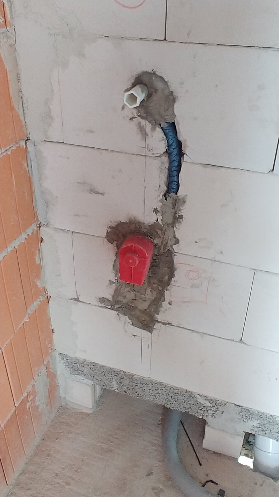 Badezimmer-Rohbau mit sichtbaren Sanitärleitungen, rotem Anschlussdeckel und blauer Leitung