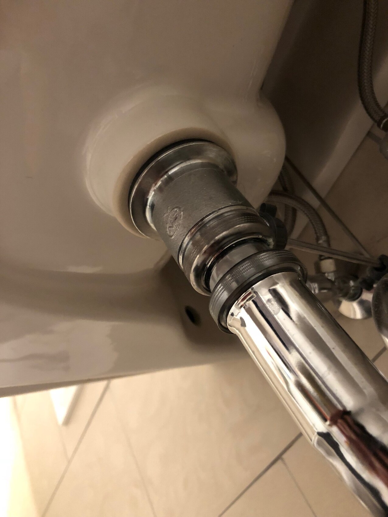 Unter dem Waschbecken sichtbarer Chrom-Siphon und Verbindungsrohr im Sanitärbereich.