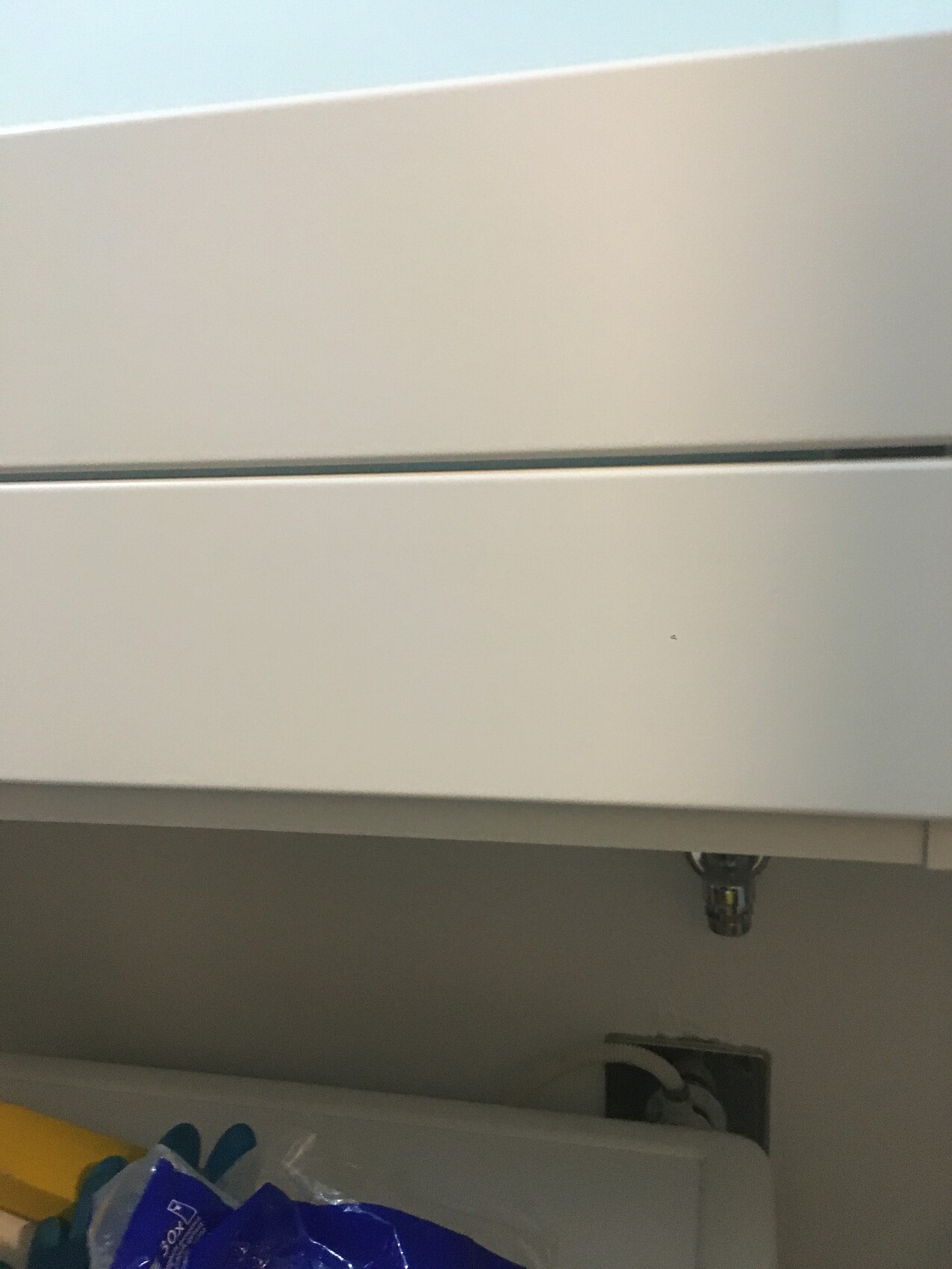 Unter der Spüle: Weißer Unterschrank, sichtbare Rohrverbindungen, Reinigungsutensilien.
