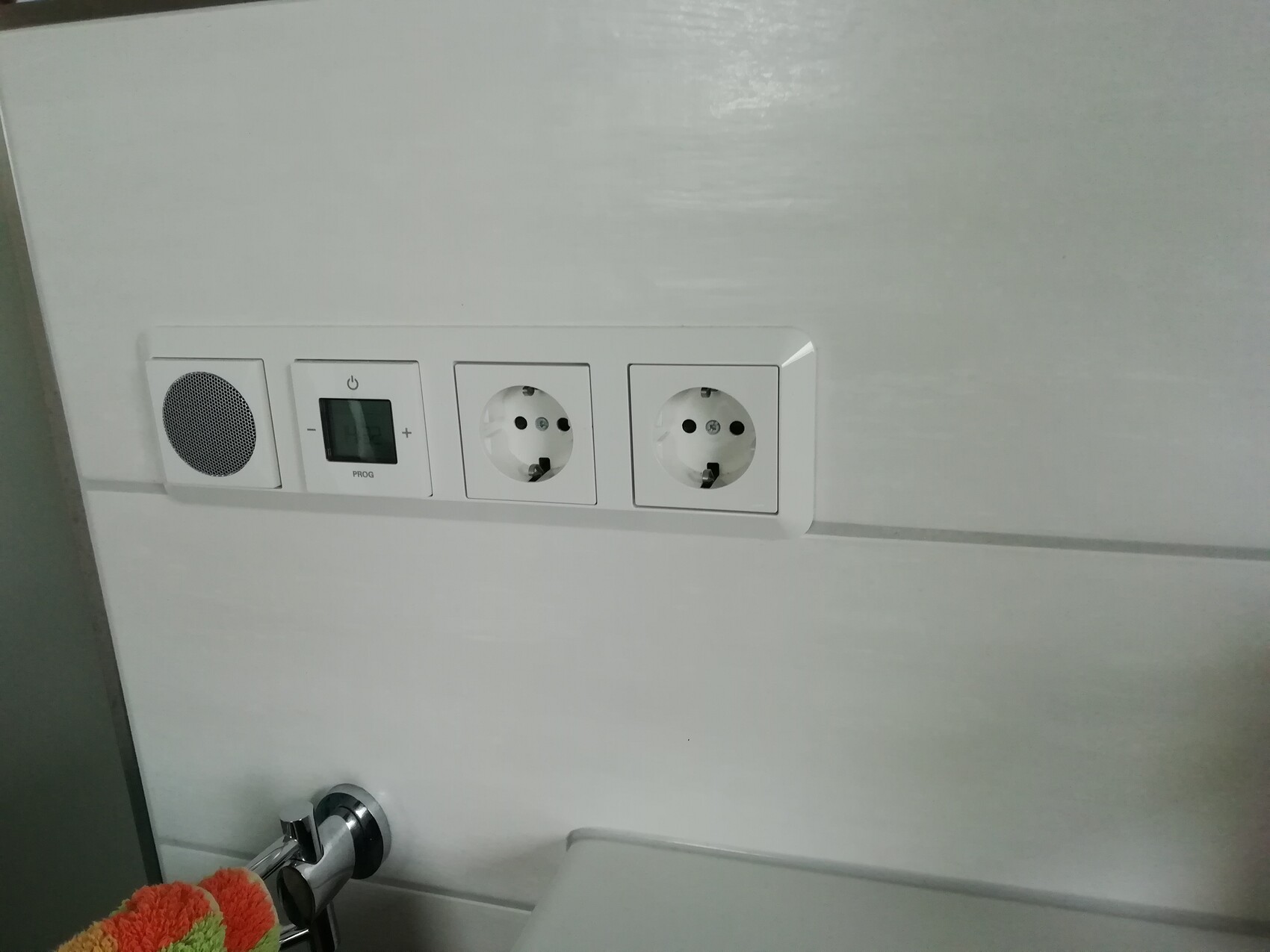 Weiße Wand mit Doppelsocket, Timer-Schalter, Lautsprecher und Handtuchhalter.