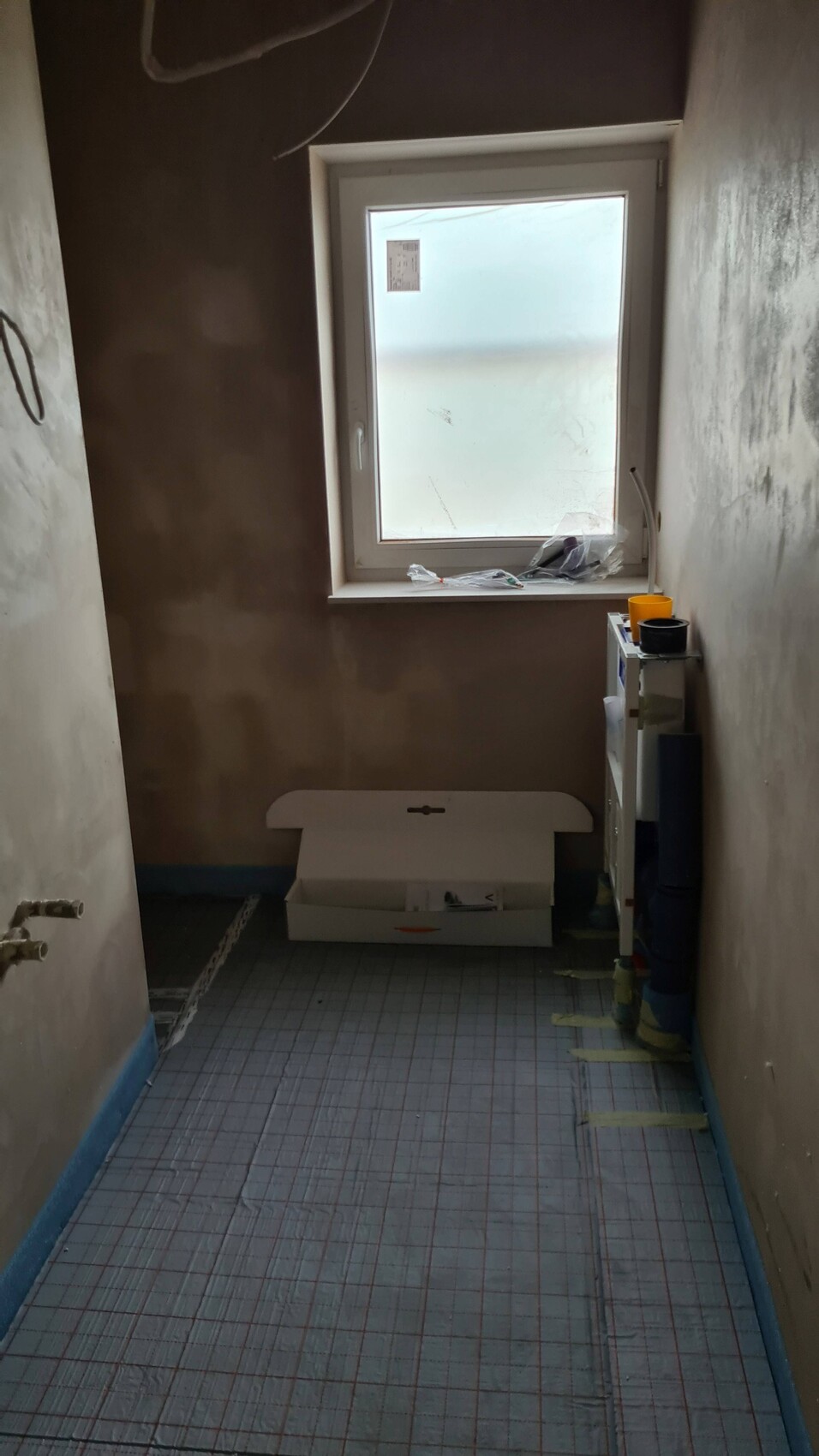Enges Badezimmer im Rohbau mit Fenster, Kartonbox und Regal voller Behälter.