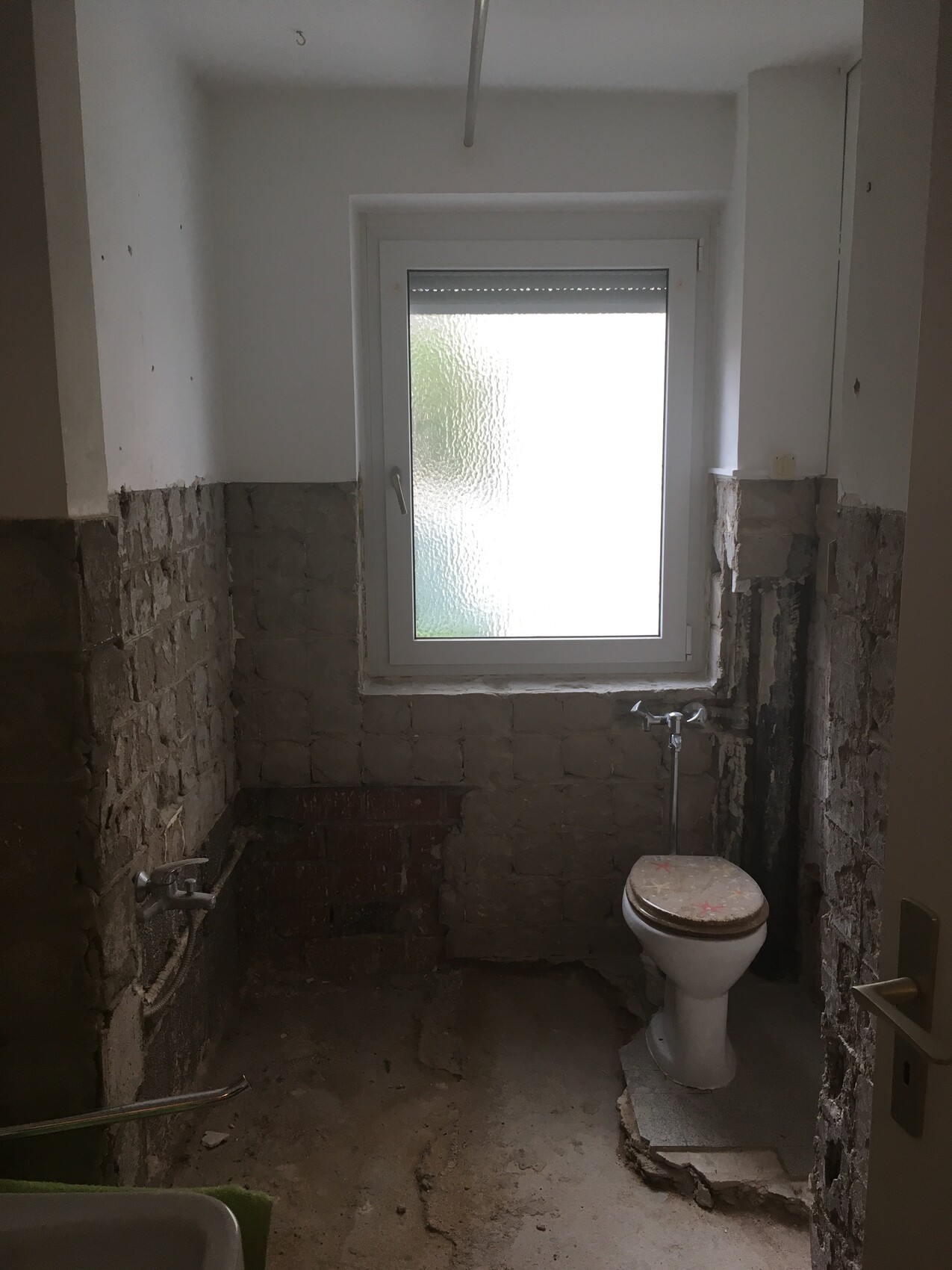Ein Badezimmer im Rohbauzustand mit Fenster, Toilette und freigelegten Ziegelwänden.