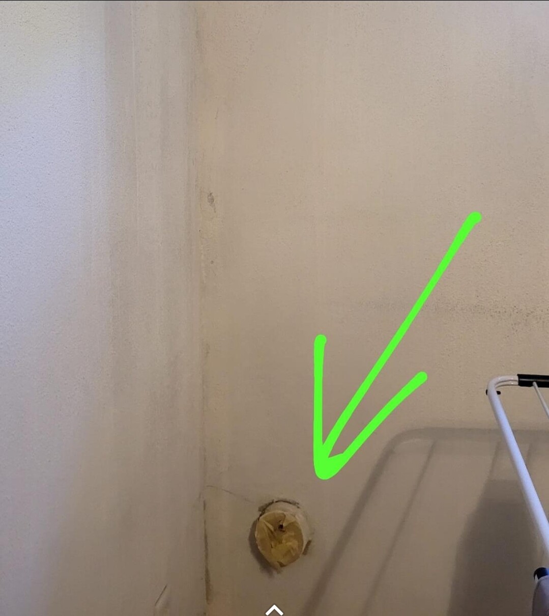 Wand-Ecke mit freier runder Rohrkappe in Gelb nahe Boden, daneben Wäscheständer.