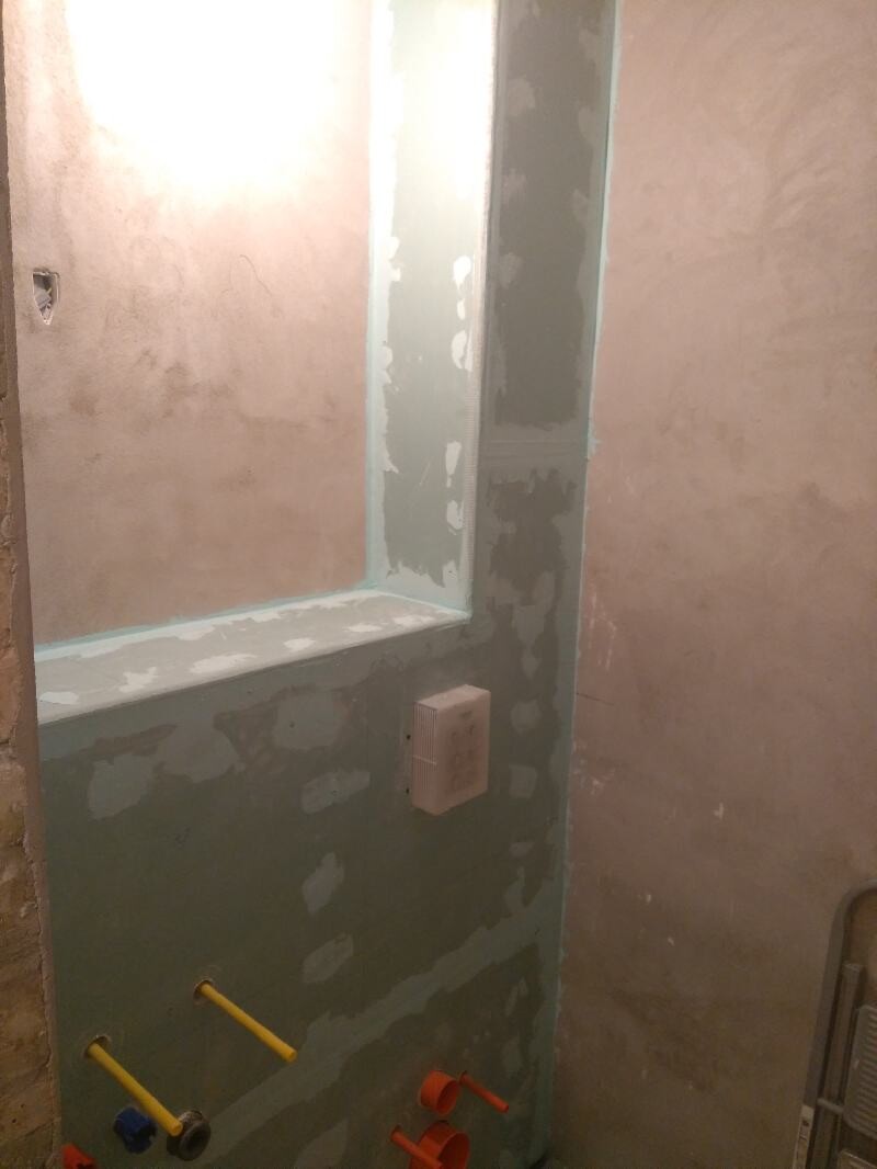 Rohbau-Badezimmer grüne Gipskartonwände, gespachtelte Flächen, sichtbare Installationen und Rohre.