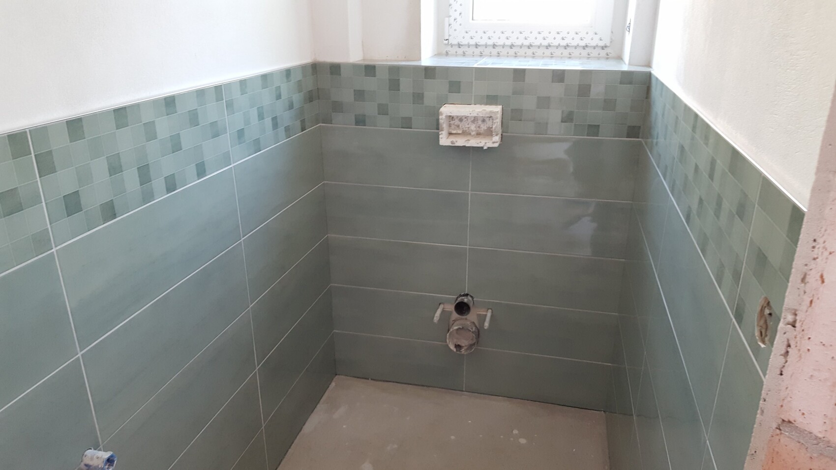 Badezimmer unter Renovierung mit gruene Wand- und Bodenfliesen, Rohinstallationen sichtbar