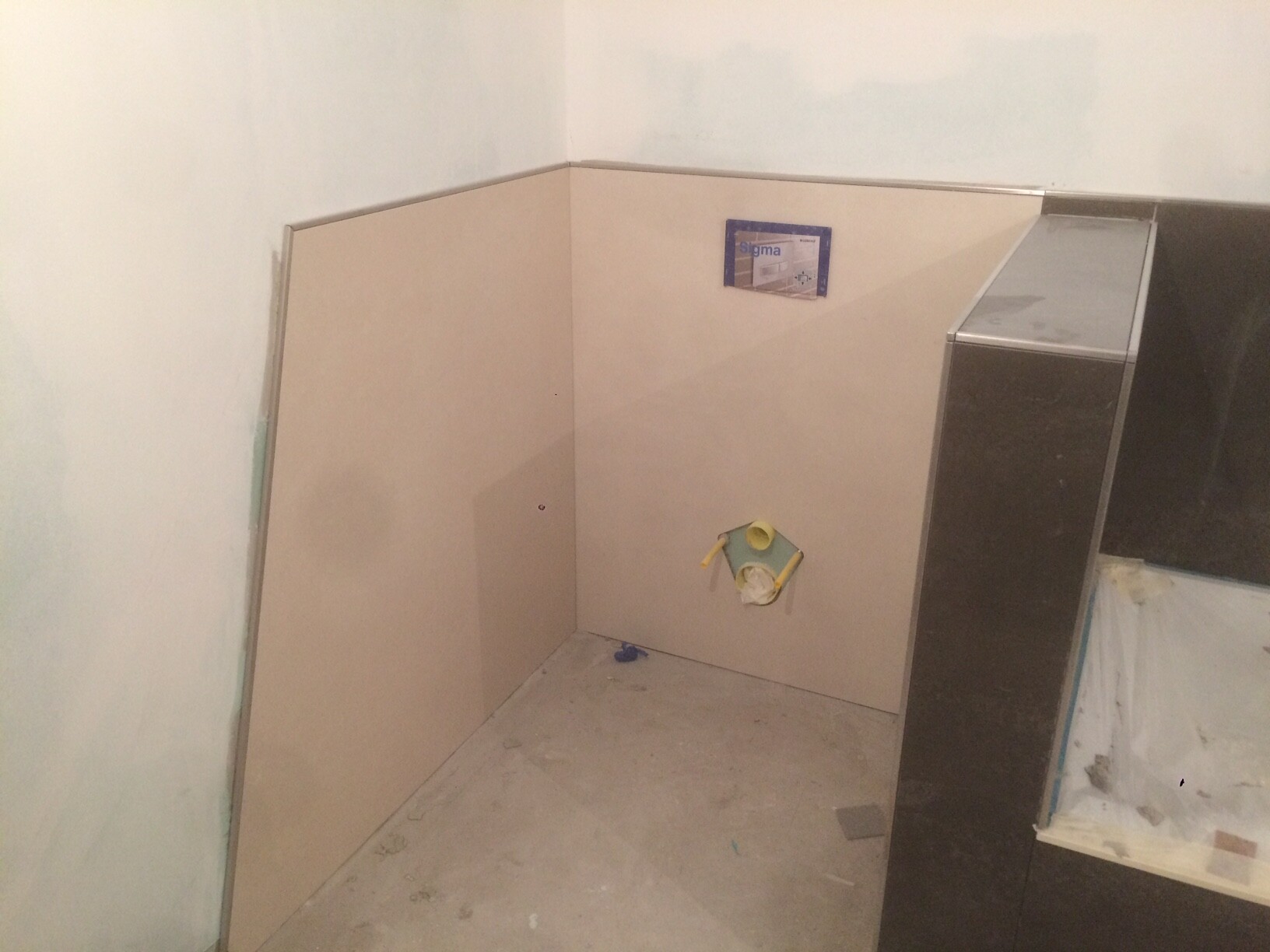 Unfertige Badezimmerbaustelle: beige Wände, offener Sanitäranschluss mit gelbem Rohr.