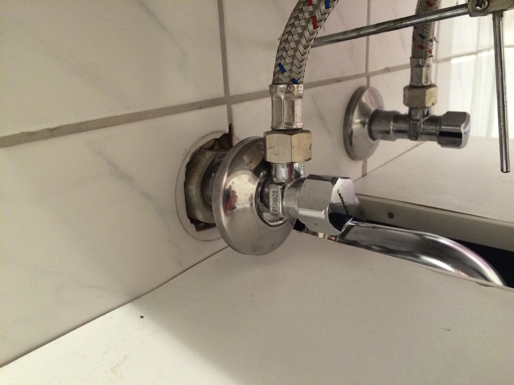 Verchromter Wasserhahn mit Absperrventil und flexibler Schlauchverbindung unter dem Waschbecken.