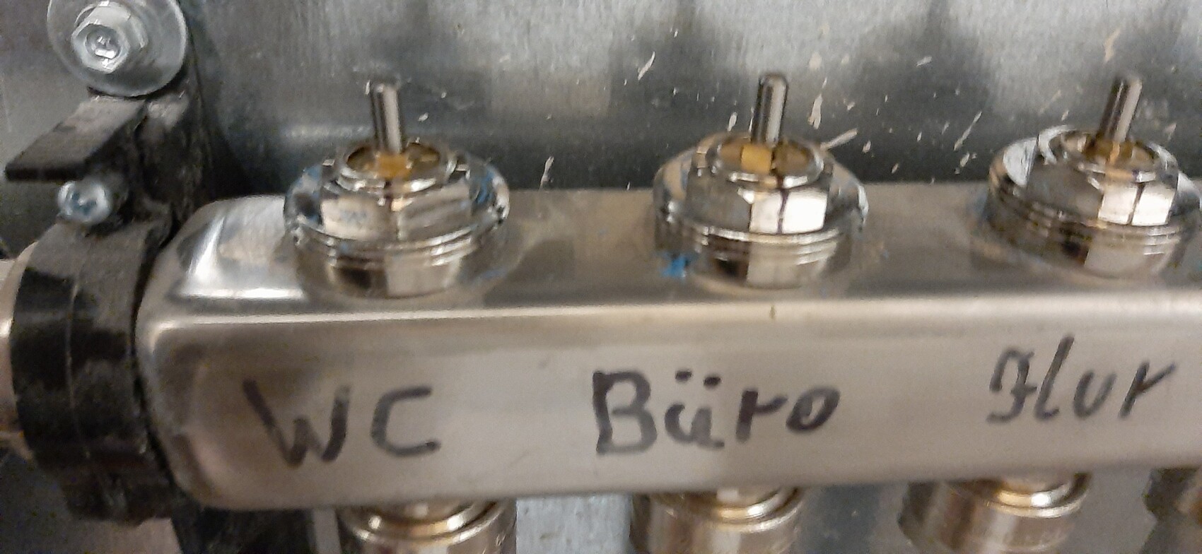 Nahaufnahme eines Metall-Verteilers mit drei Ventilknöpfen; Frontplatte mit der Bezeichnung 'WC'