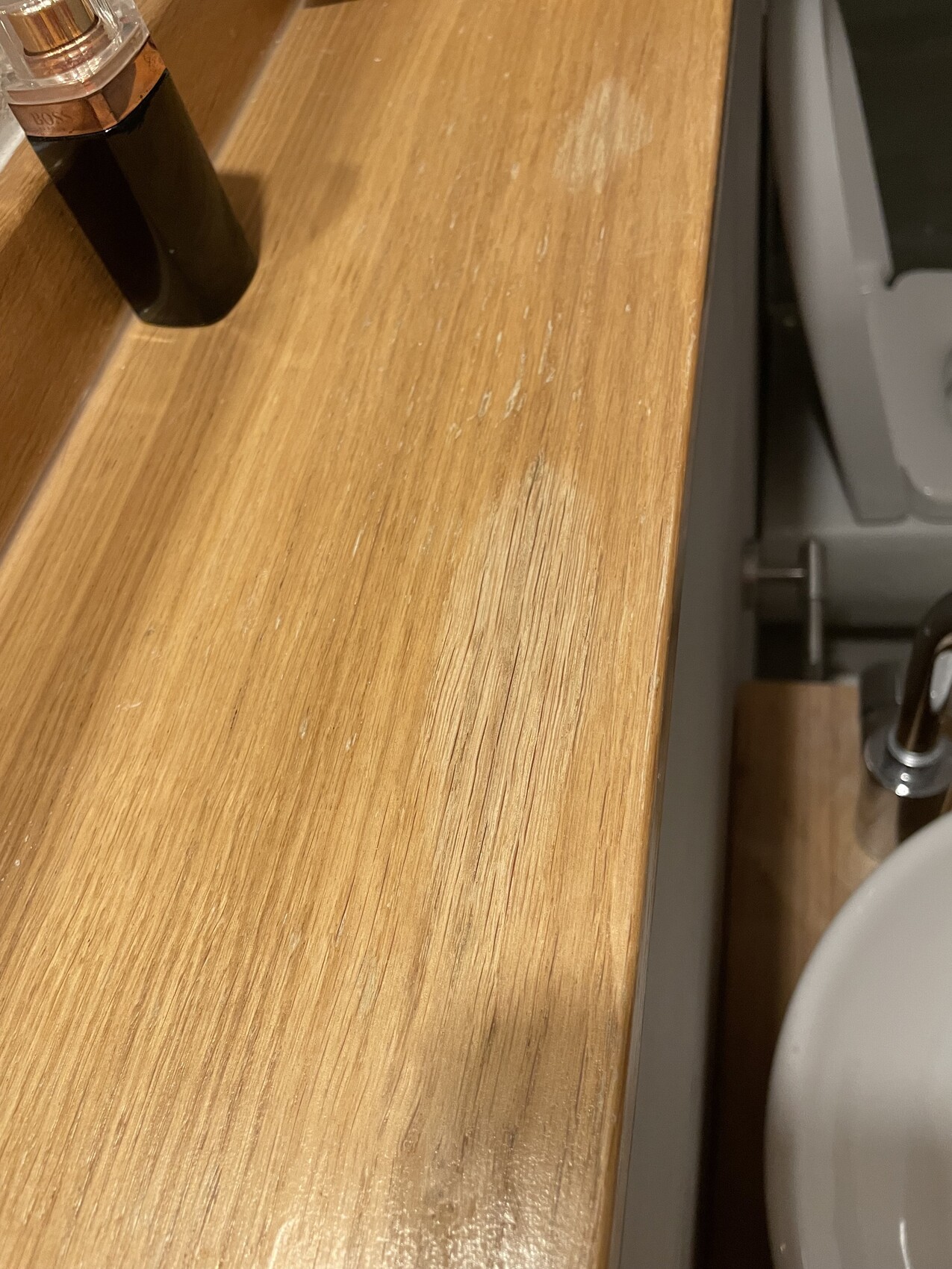 Holz-Waschtisch mit dunkler Parfumflasche am Rand, Badezimmer-Umgebung.