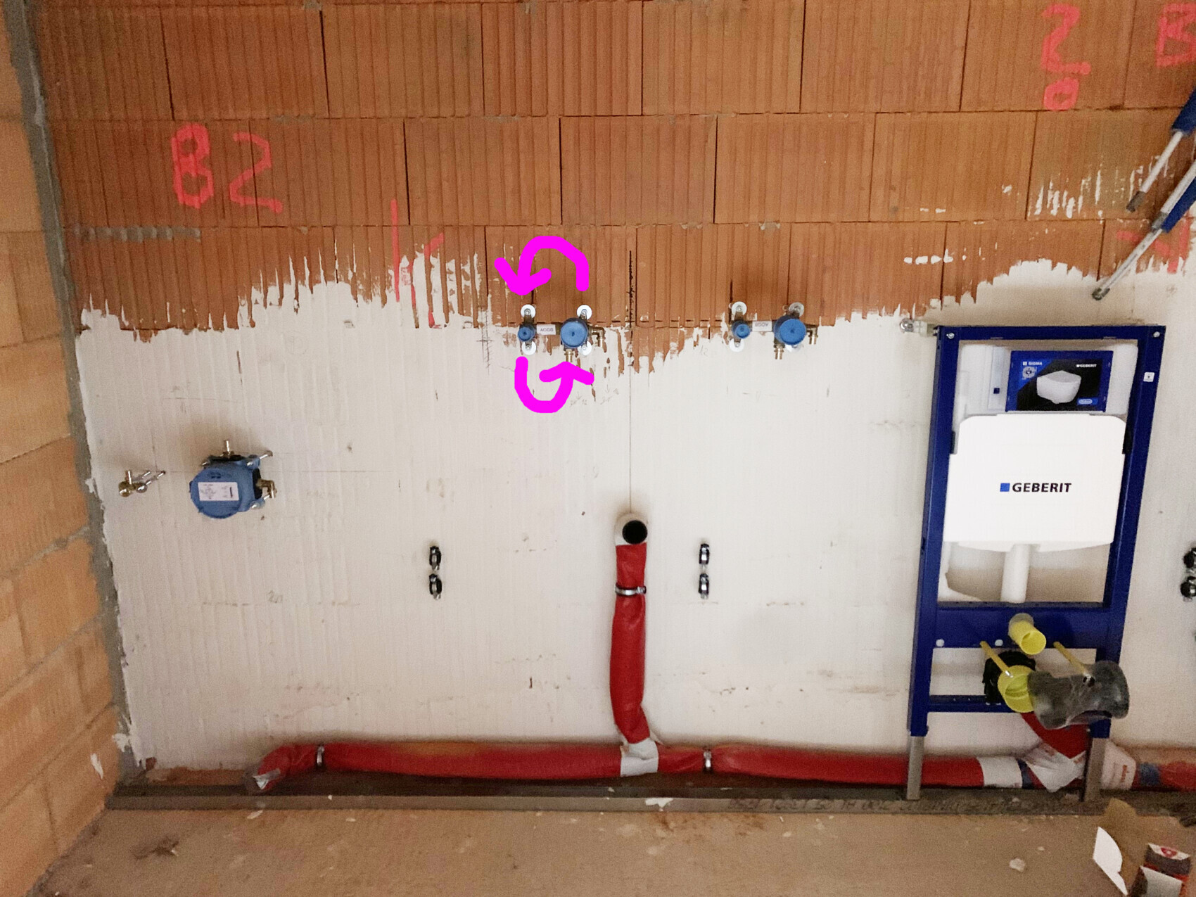 Rohbau-Wandinstallation: Geberit-Spülkasten rechts, rote Rohre, blaue Absperrventile.
