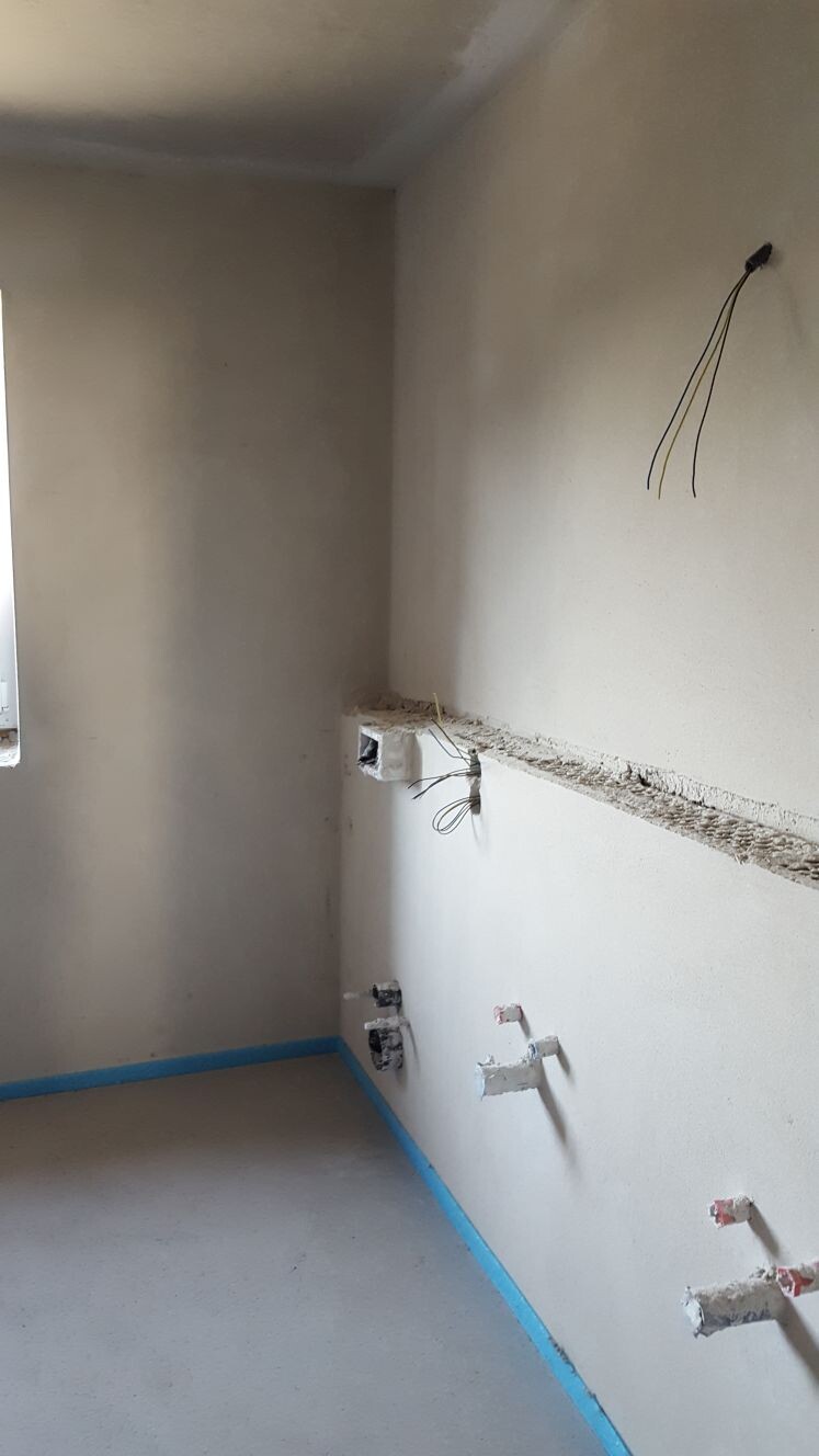 Badezimmer im Rohbau mit freiliegenden Wasserleitungen und Kabeln an der Wand