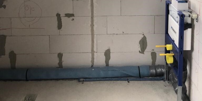 Blaue Rohrleitung liegt am Boden; rechts eine Wandvorrichtung mit zwei gelben Griffen.
