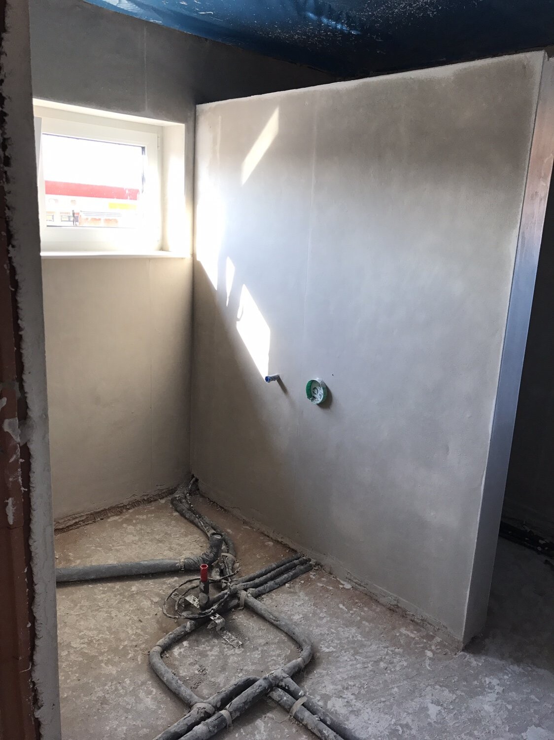 Unbearbeiteter Badezimmerbereich mit Rohbauwänden, sichtbaren Rohren und Fenster.