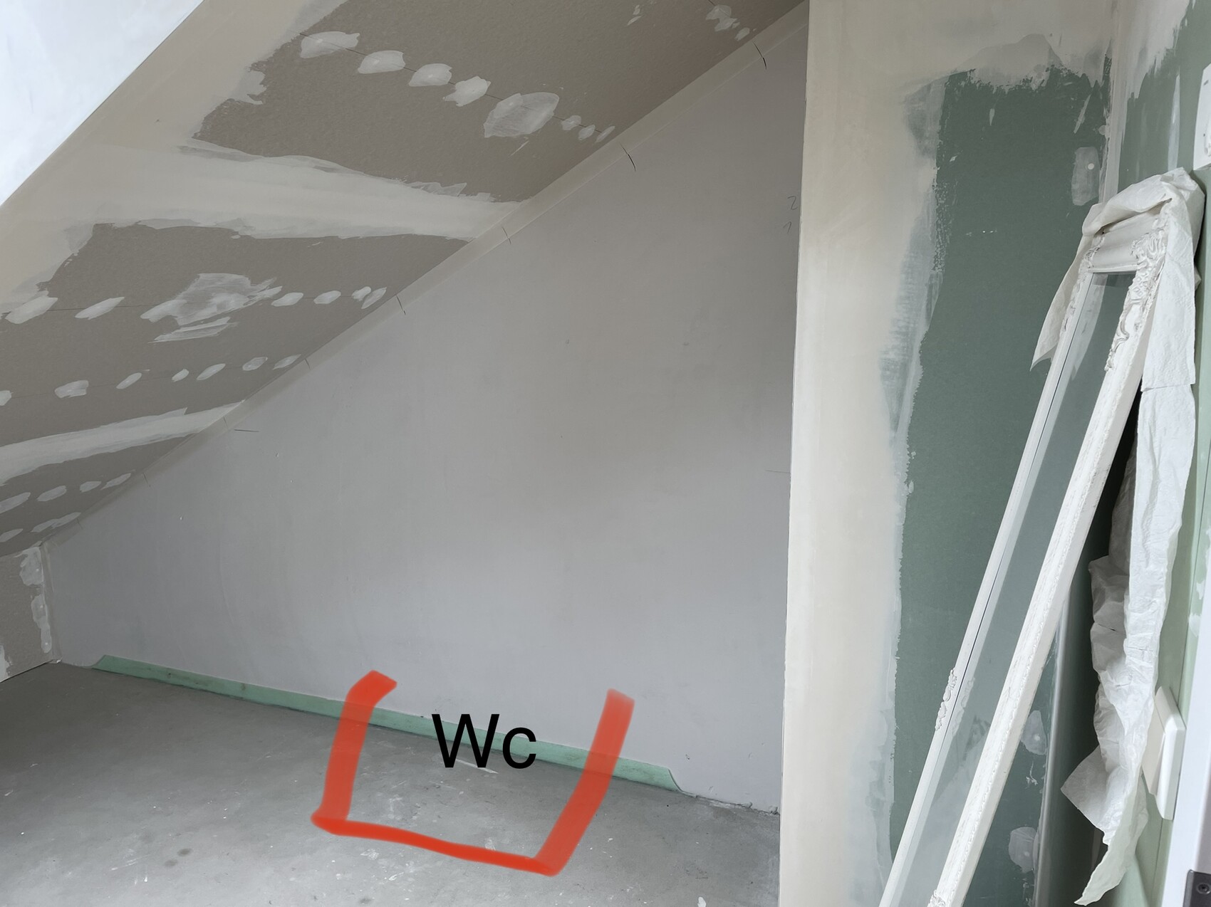 Unfertiger Dachgeschossraum mit schräger Decke; Boden markiert WC-Bereich.