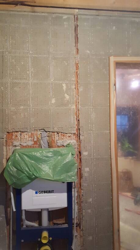 Offene Wand mit Geberit-Sanitärrahmen und grüner Abdeckplane.