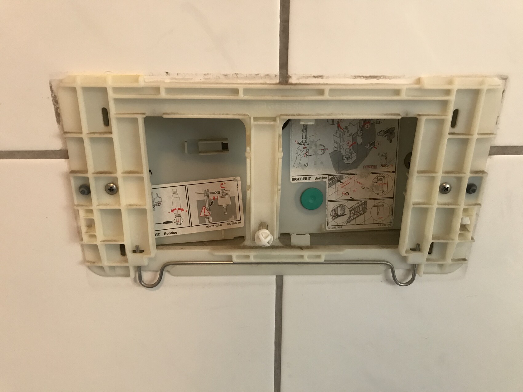Versteckter Spülkasten-Montagerahmen in Fliesenwand mit Bildanleitungen und grünem Knopf.