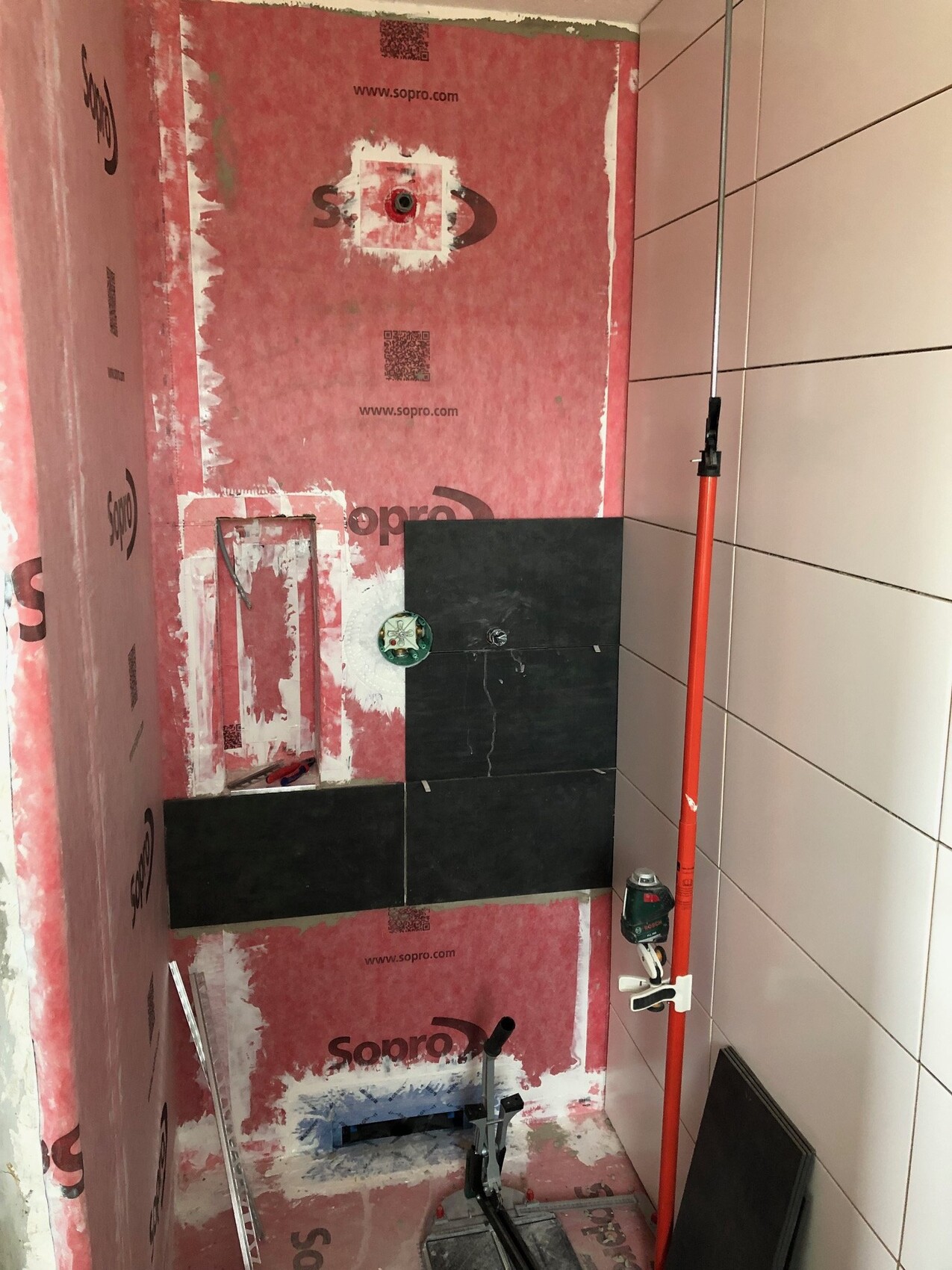 Badezimmerunterbau im Bau: rosa Dämmung, schwarze Fliesen, Sanitärinstallationen
