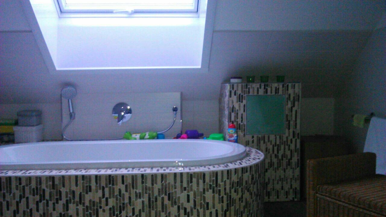 Badezimmer im Dachgeschoss mit Badewanne, Mosaikfliesen und Dachfenster.