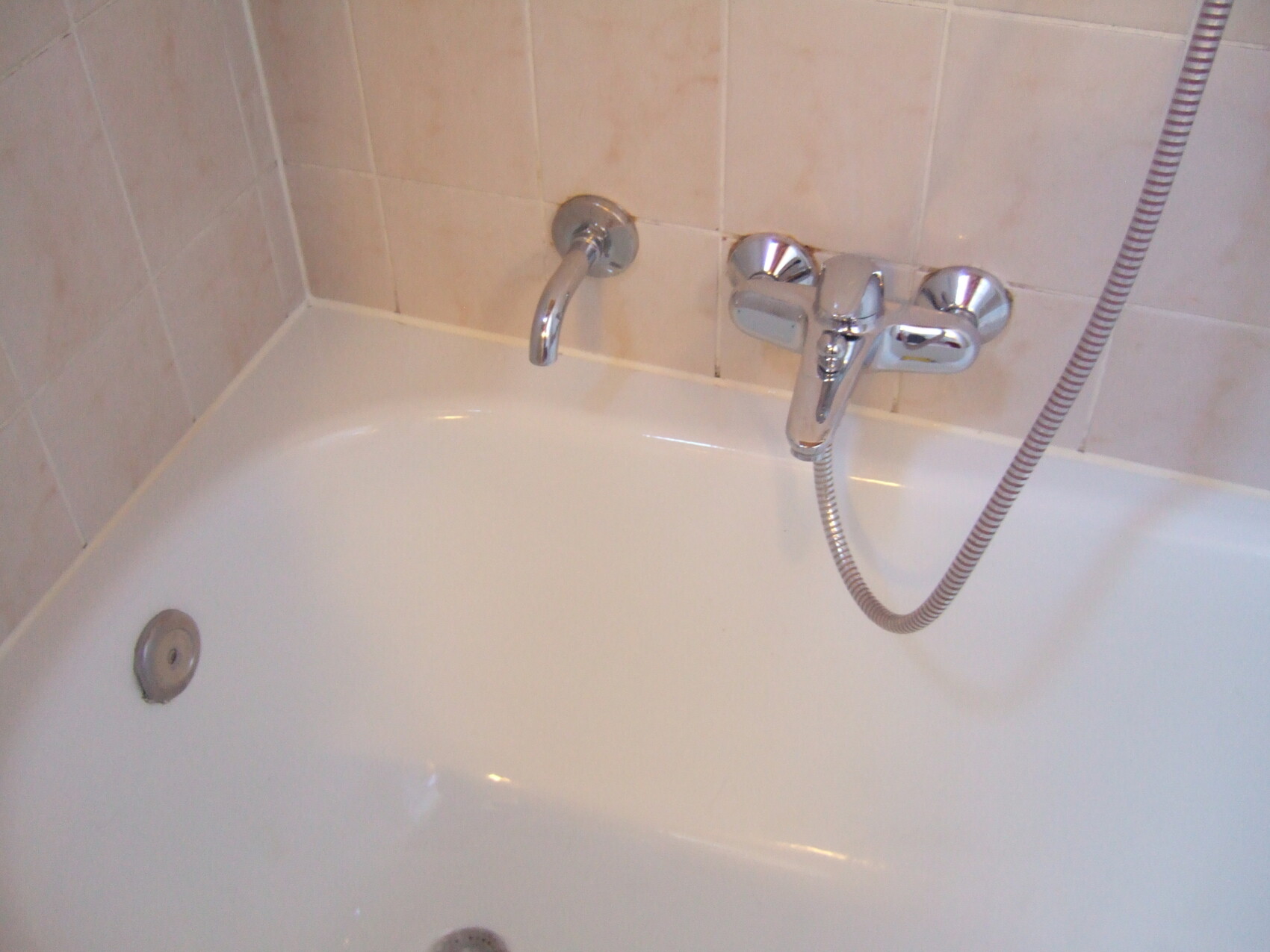 Badewanne mit Chrom-Armatur, Brausehalter und Duschschlauch vor hellen Fliesen