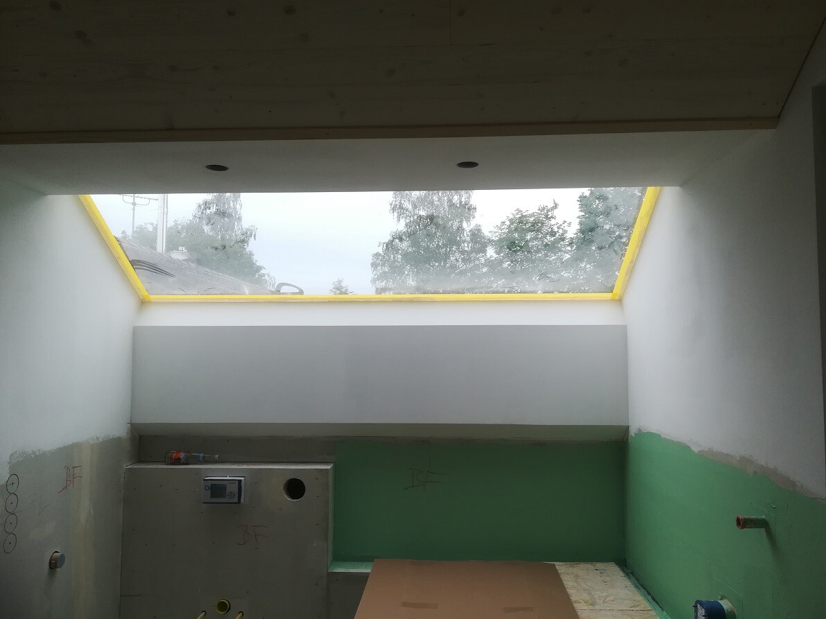 Unfertiger Innenraum mit gelbem Dachfensterrahmen, grüne und weiße Wände, Baustelle.