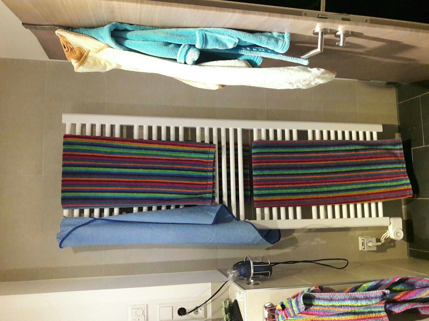 Badezimmer mit Heizkörper, bunten Handtüchern und Fliesenboden