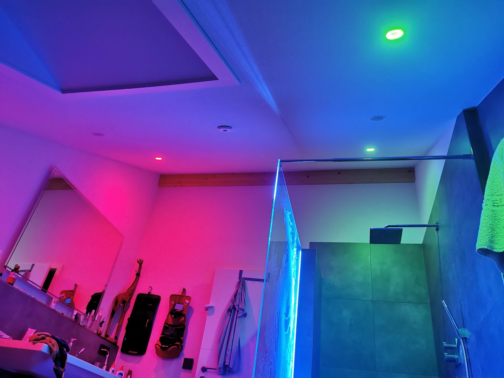 Badezimmer mit farbigem Neonlicht, Glasdusche und Badzubehör mit Handtüchern.