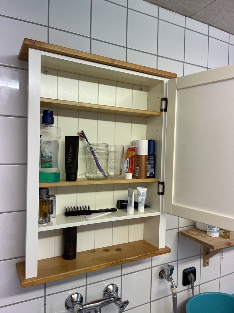 Offene Badezimmer-Ablage mit Zahnpflegeprodukten, Zahnbürsten, Cremes und Glasbehälter.