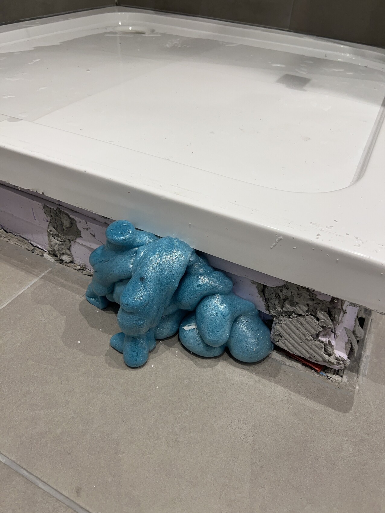 Blauer Montageschaum quillt aus der Fuge unter der Badewannenkante, daneben beschädigte Wand.