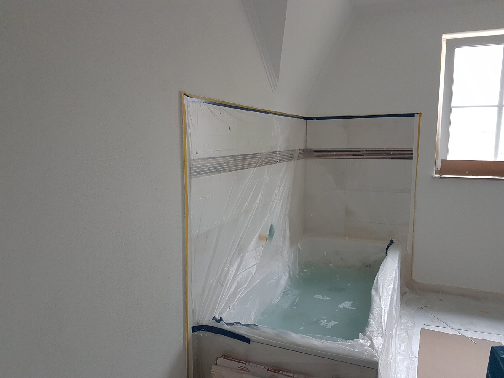 Badezimmer im Bau mit verpackter Badewanne, Fliesenwand und Fenster