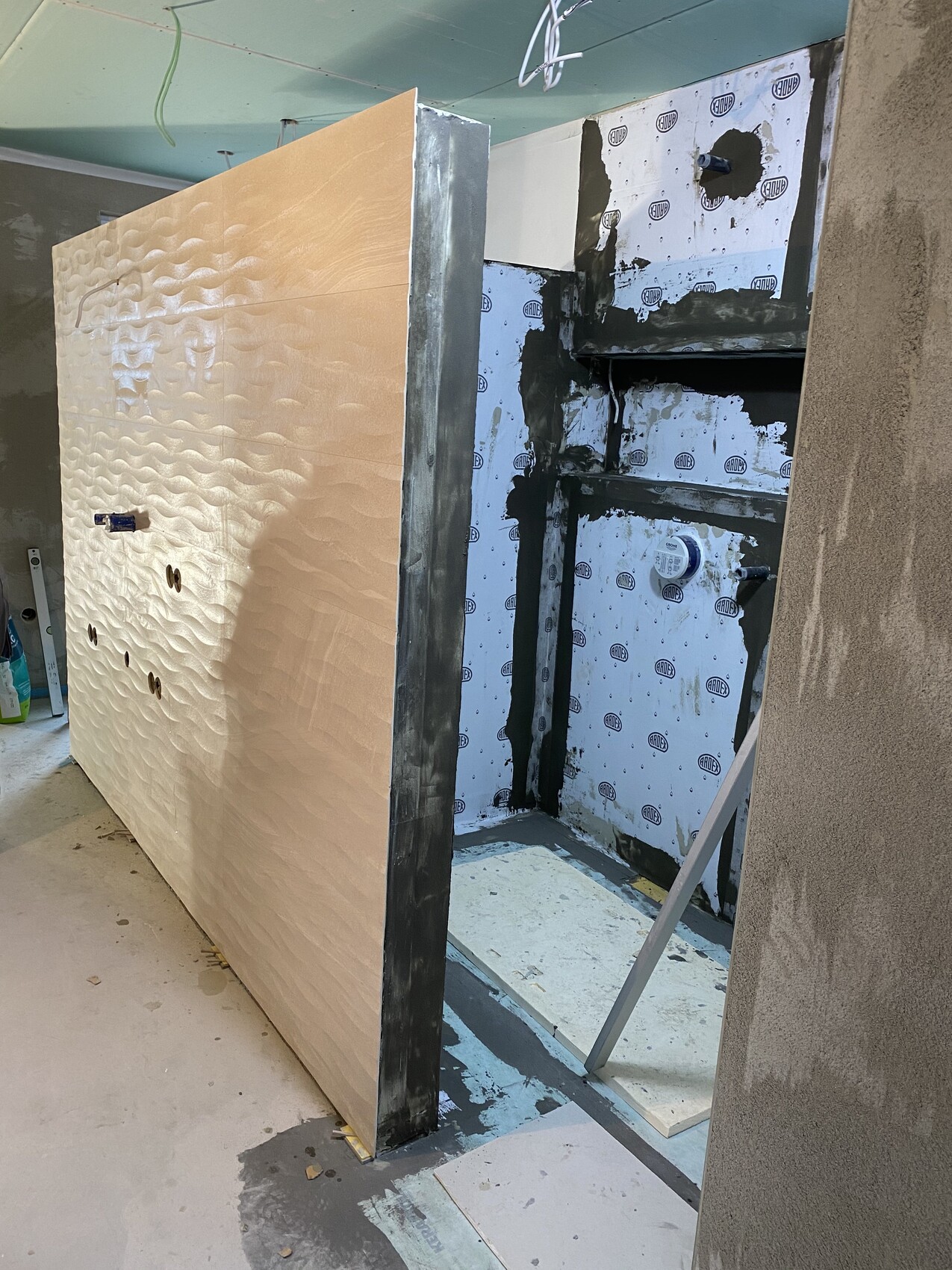 Große beige Paneelwand mit Wellenstruktur in Baufortschritt, dahinter freigelegte Wand und Dämmung.
