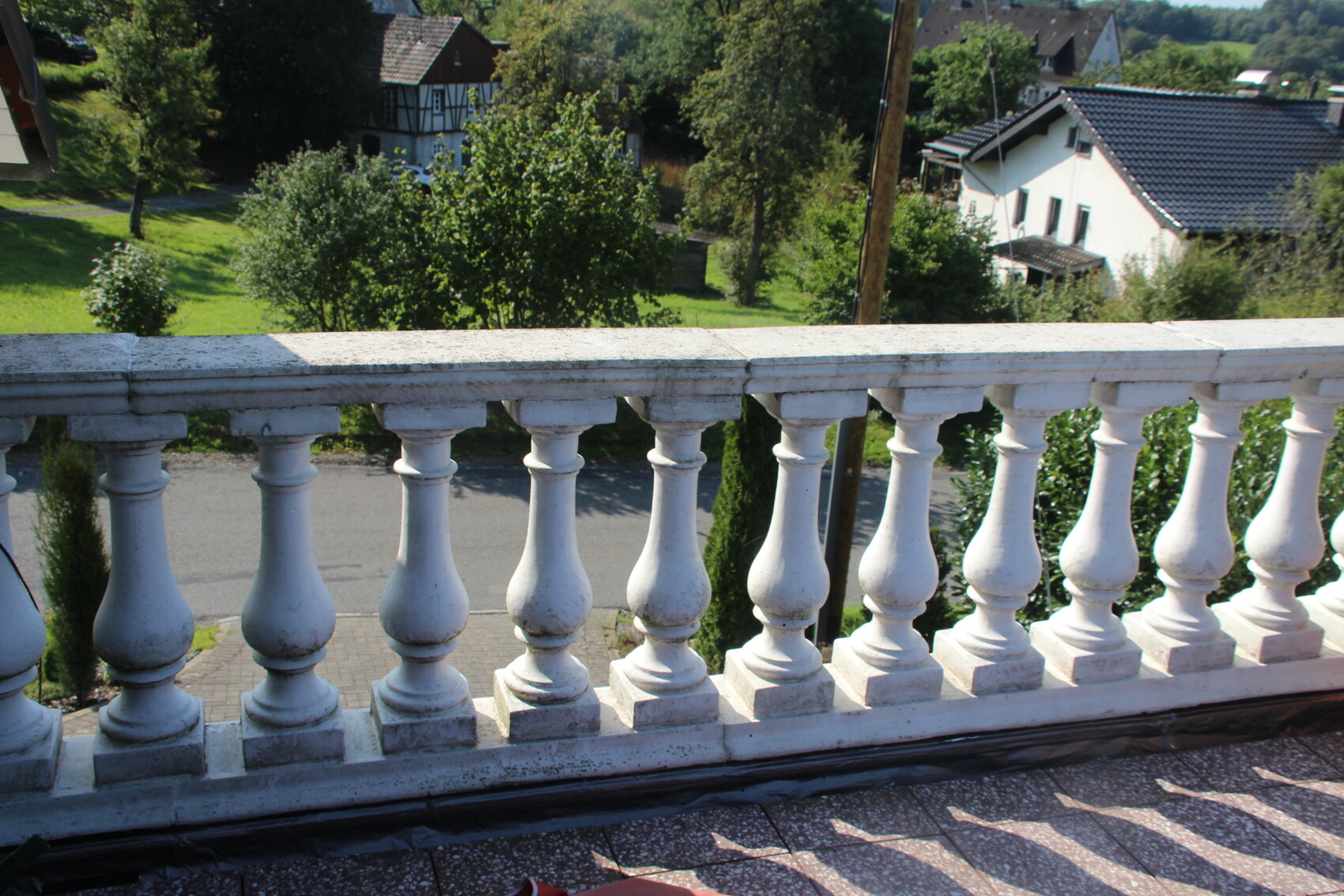 Weiße Balustrade am Balkon mit grünem Garten und Häusern im Hintergrund