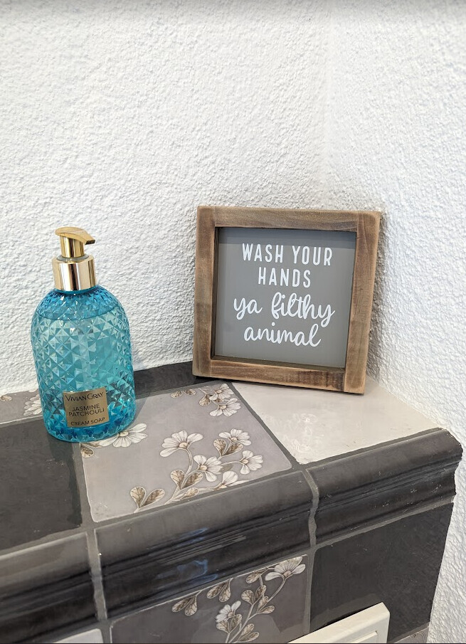 Blaue Seife mit Goldspender neben Holzrahmen-Schild "WASH YOUR HANDS ya filthy animal".