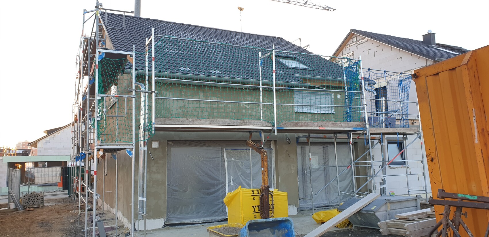 Zweistöckiges Haus auf Baustelle mit Gerüst, grünen Netzen und Folienabdeckung.