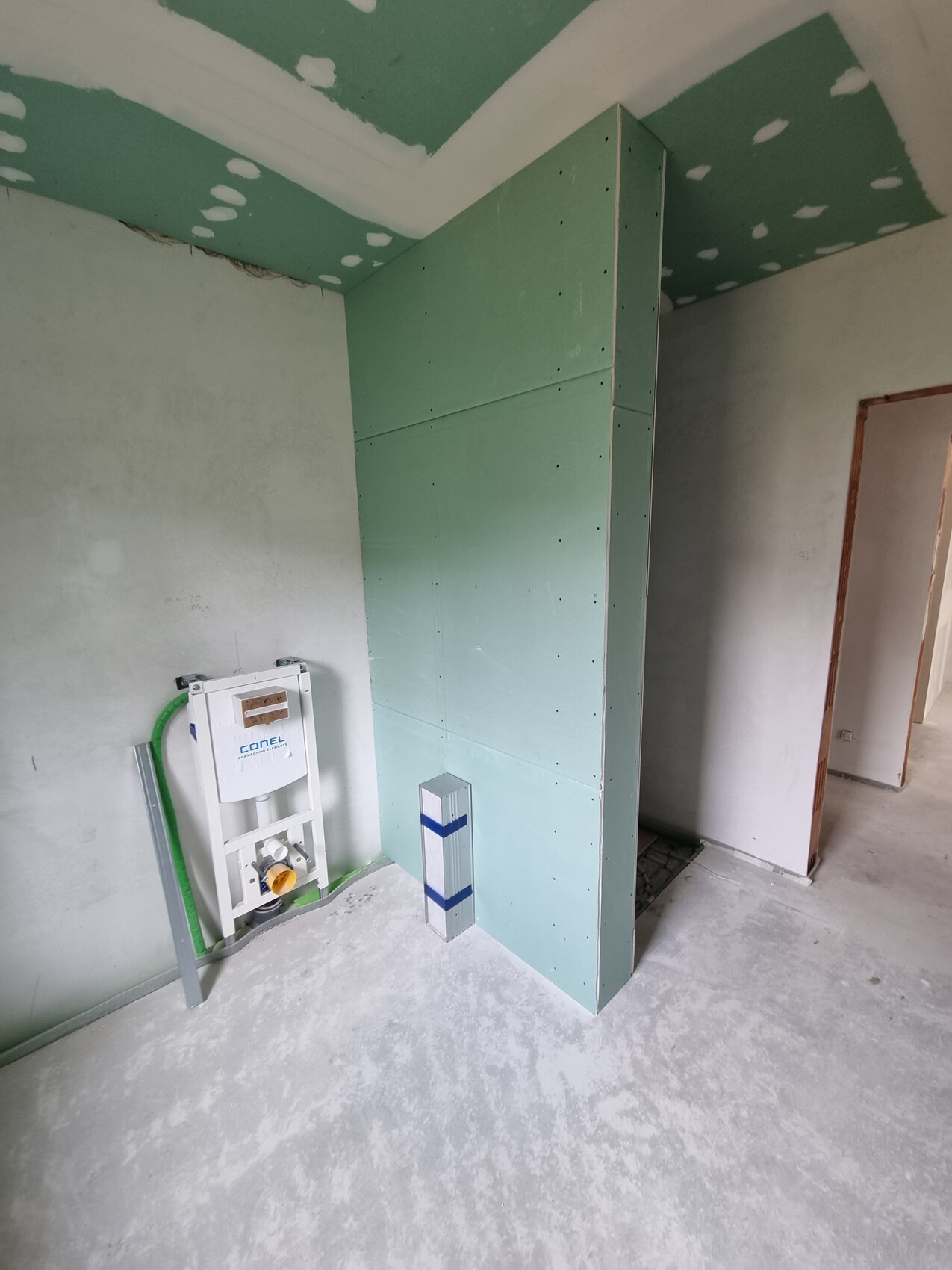 Baustelle: grüne Trockenbauwand, Spülkasten-Installation; offener Durchgang rechts.