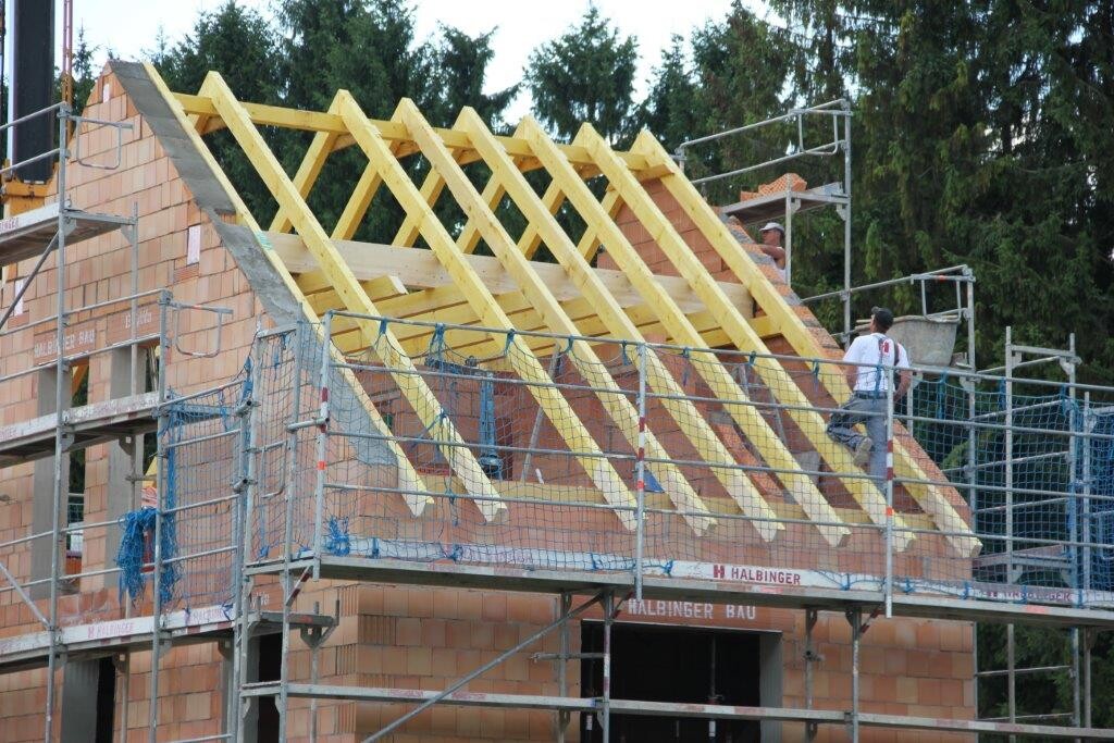 Baustelle mit Holz-Dachstuhlrahmen auf Rohbau, Gerüst um das Haus