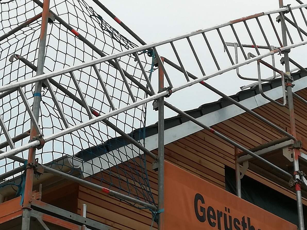 Metallgerüst mit Sicherheitsnetzen an einem Holzbau, orangefarbenes Banner sichtbar