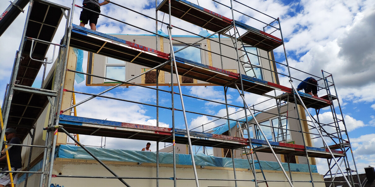 Bauarbeiter arbeiten am Rohbau eines mehrstöckigen Hauses auf dem Gerüst, blauer Himmel.