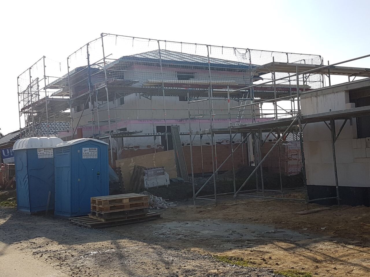Baugerüstete Baustelle um ein Haus mit Gerüst, Containern und Holzpaletten
