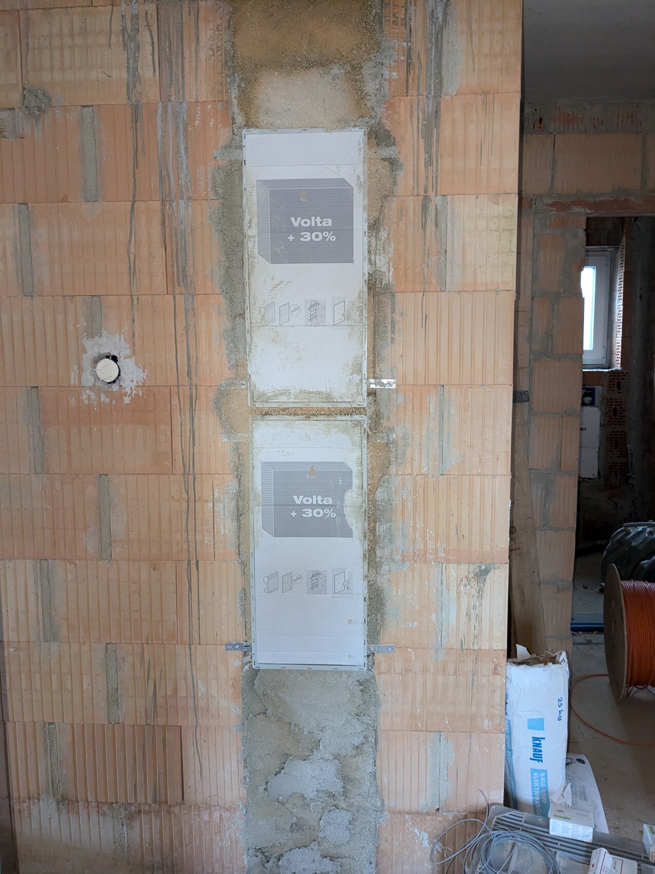 Zwei Verteilerschränke an einer Ziegelwand im Rohbau, Baustelle mit Kabelrollen.