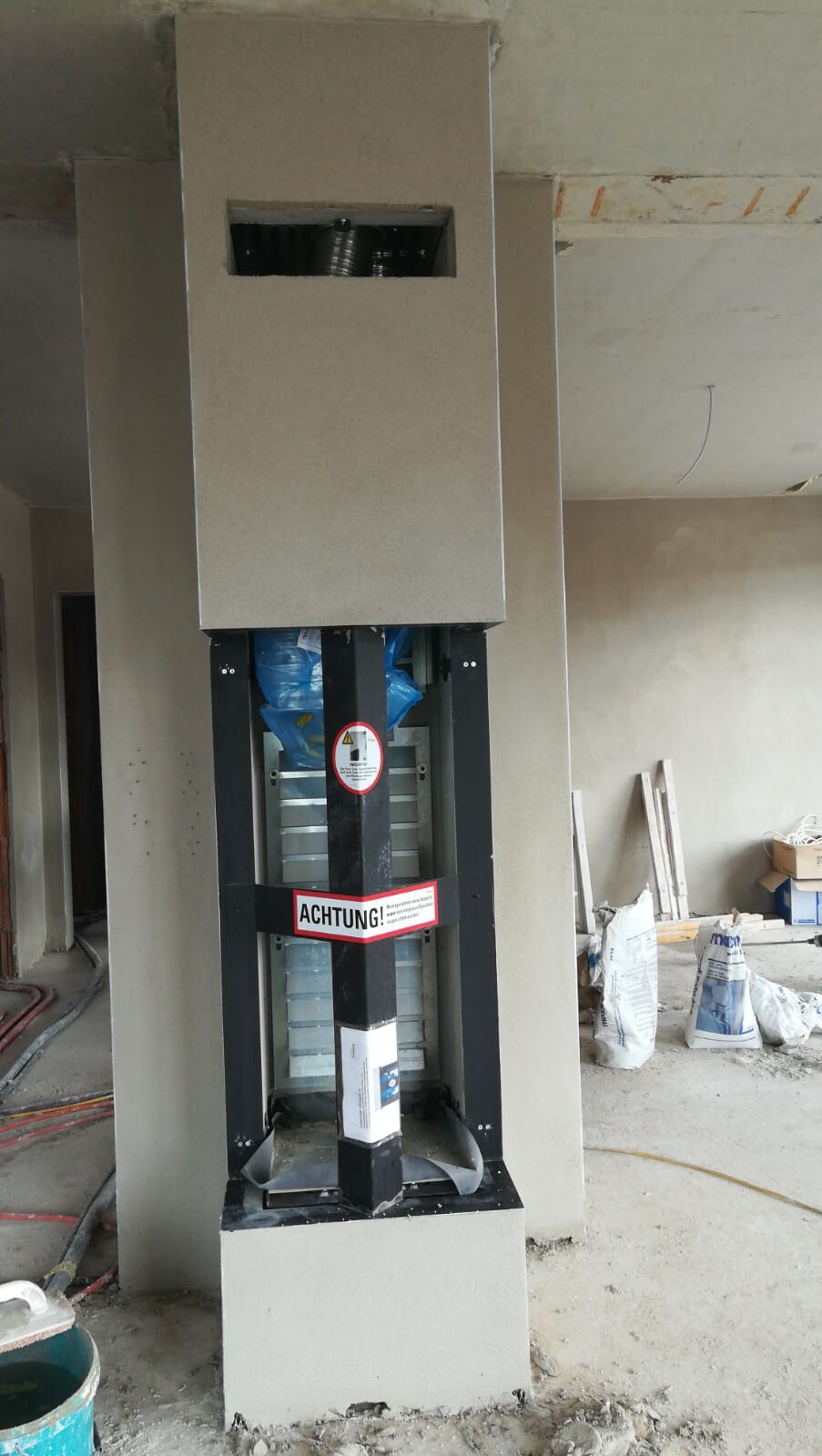 Baustellen-Aufzug in offener Schachtführung mit Warnschild ACHTUNG.