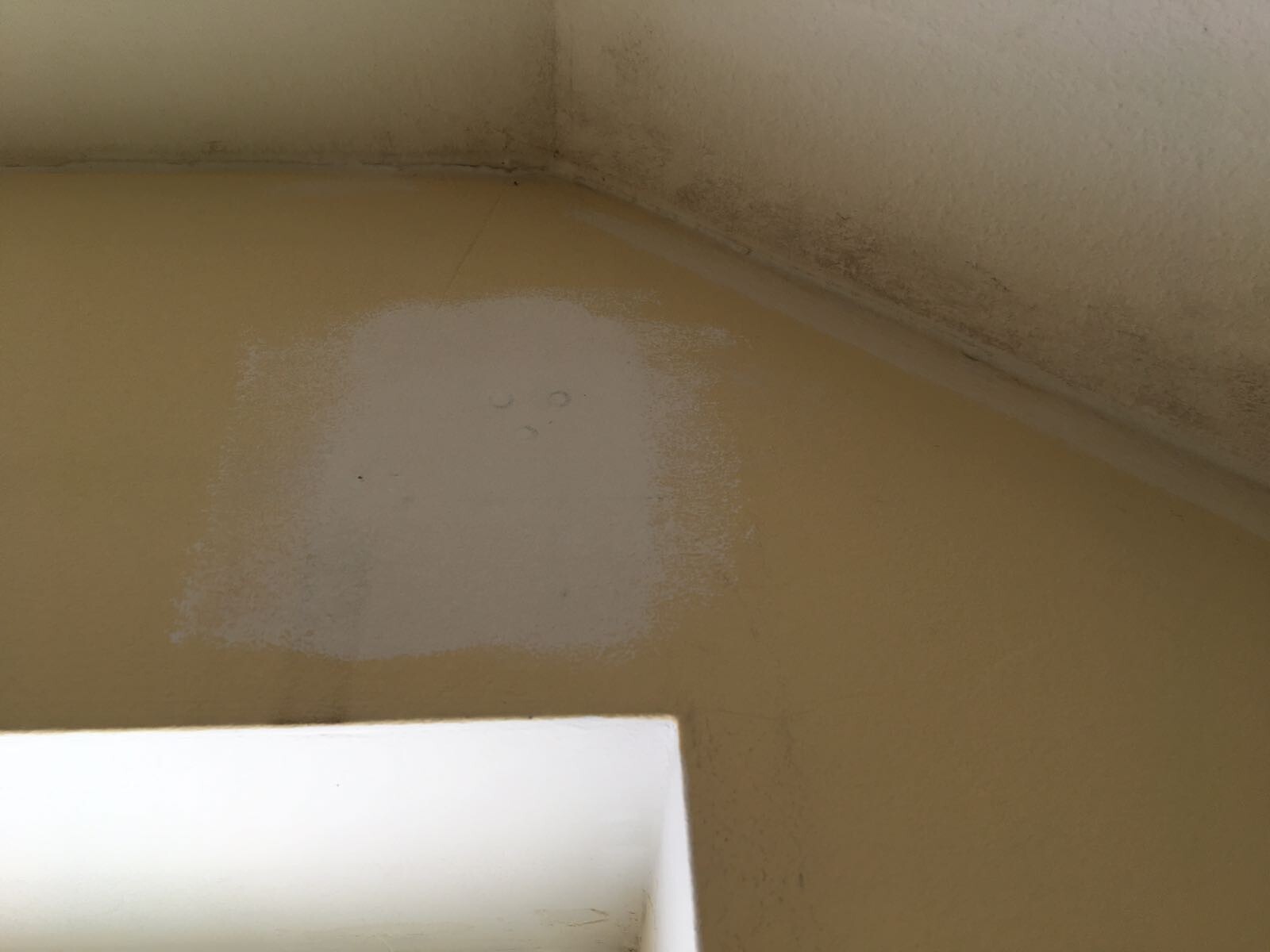 Eckwand mit weißem Reparaturpatch an gelber Wand neben Fenster