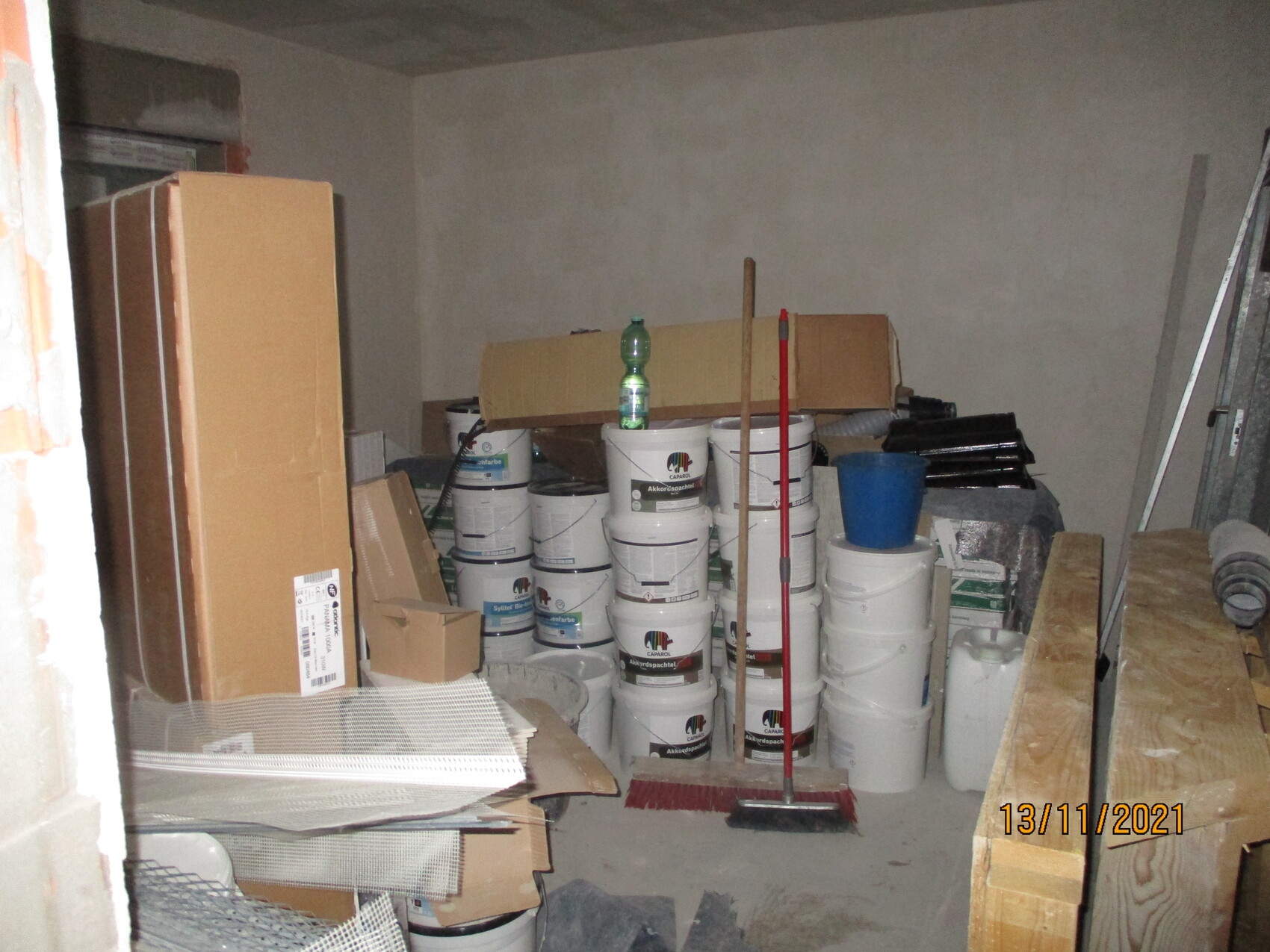 Unordentlicher Abstellraum voller Farbfässer, Kartons, Besenstiel und Holzlatten.