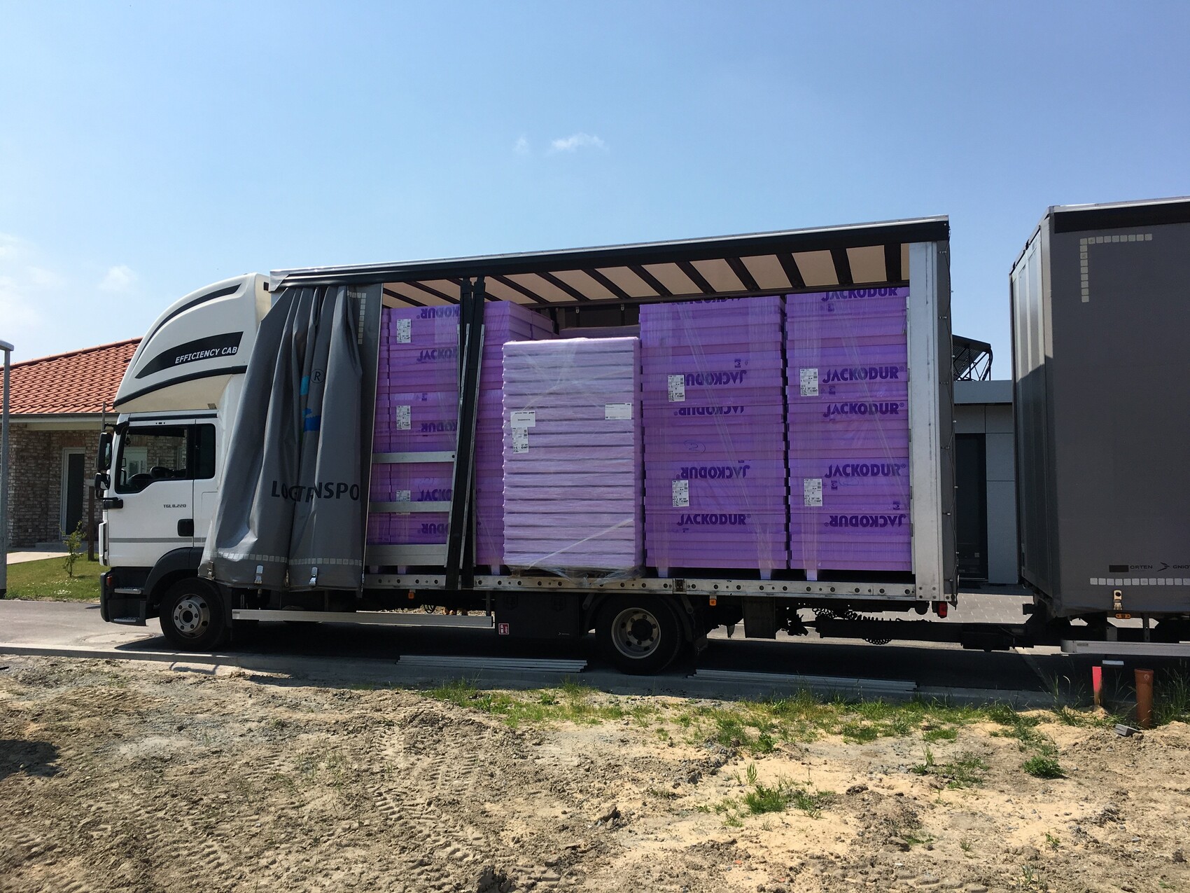 Lastwagen mit offener Seitenwand beladen mit gestapelten violetten JACKODUR-Dämmplatten im Trailer.