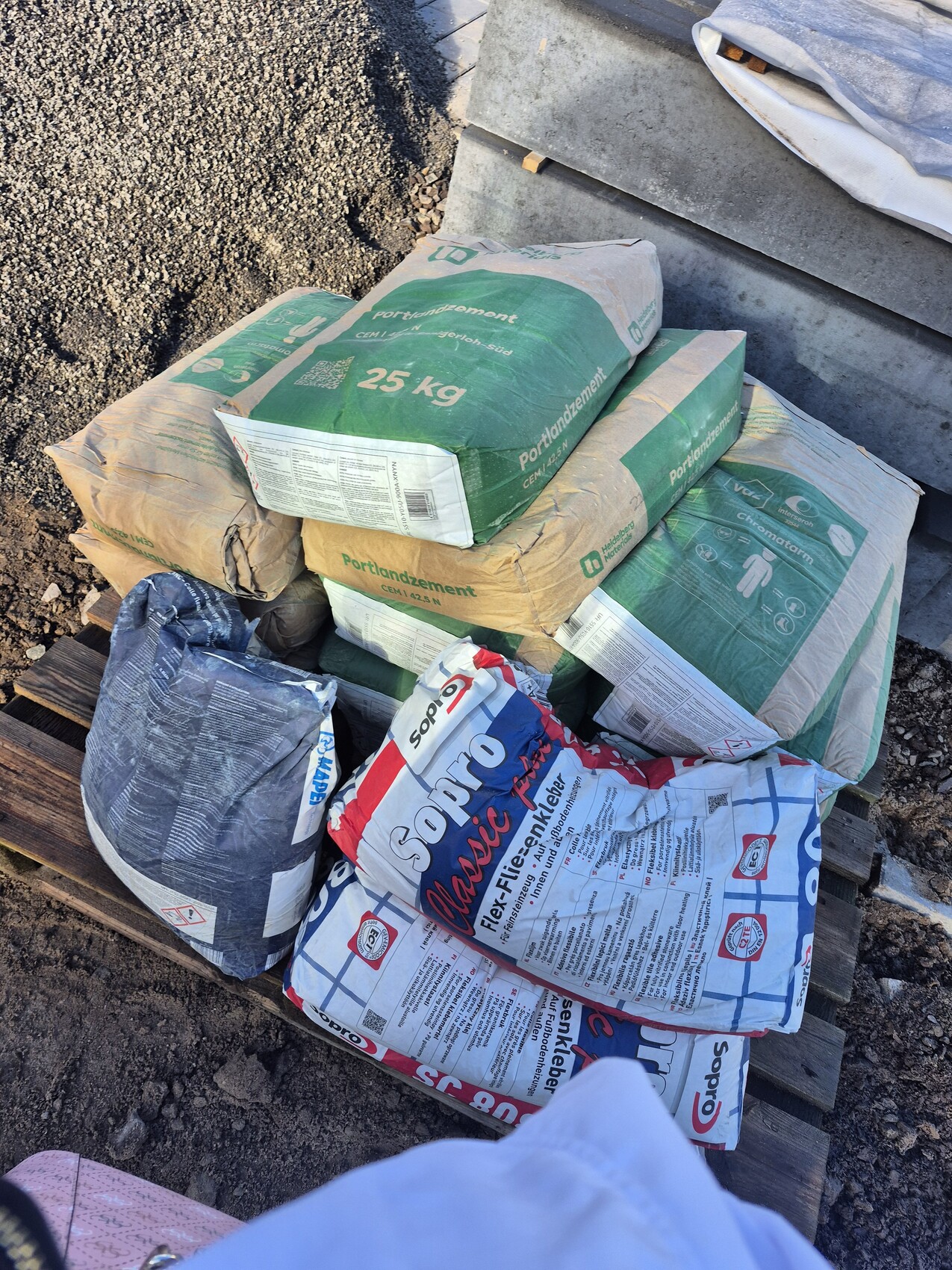 Mehrere Zementsaecke und Baumaterialien auf einer Holzpalette auf einer Baustelle