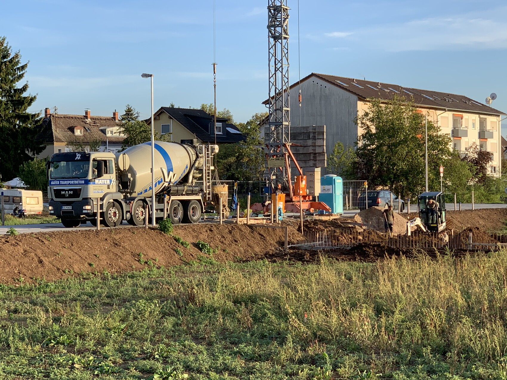 Baustelle mit Zementmischwagen, Baukran, Erdarbeiten und Wohnhäusern im Hintergrund.