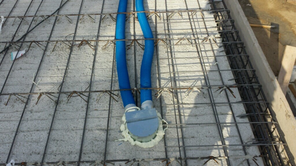 Bauplatte mit Bewehrung, zwei blaue Schläuche führen zu rundem Rohrdurchlass mit Dichtmasse.