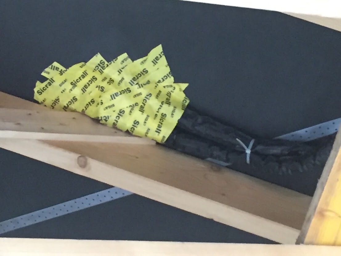 Holzbalken über dunkler Fläche; gelbes Warnband um einen schwarzen Gegenstand mit Kabelbinder.