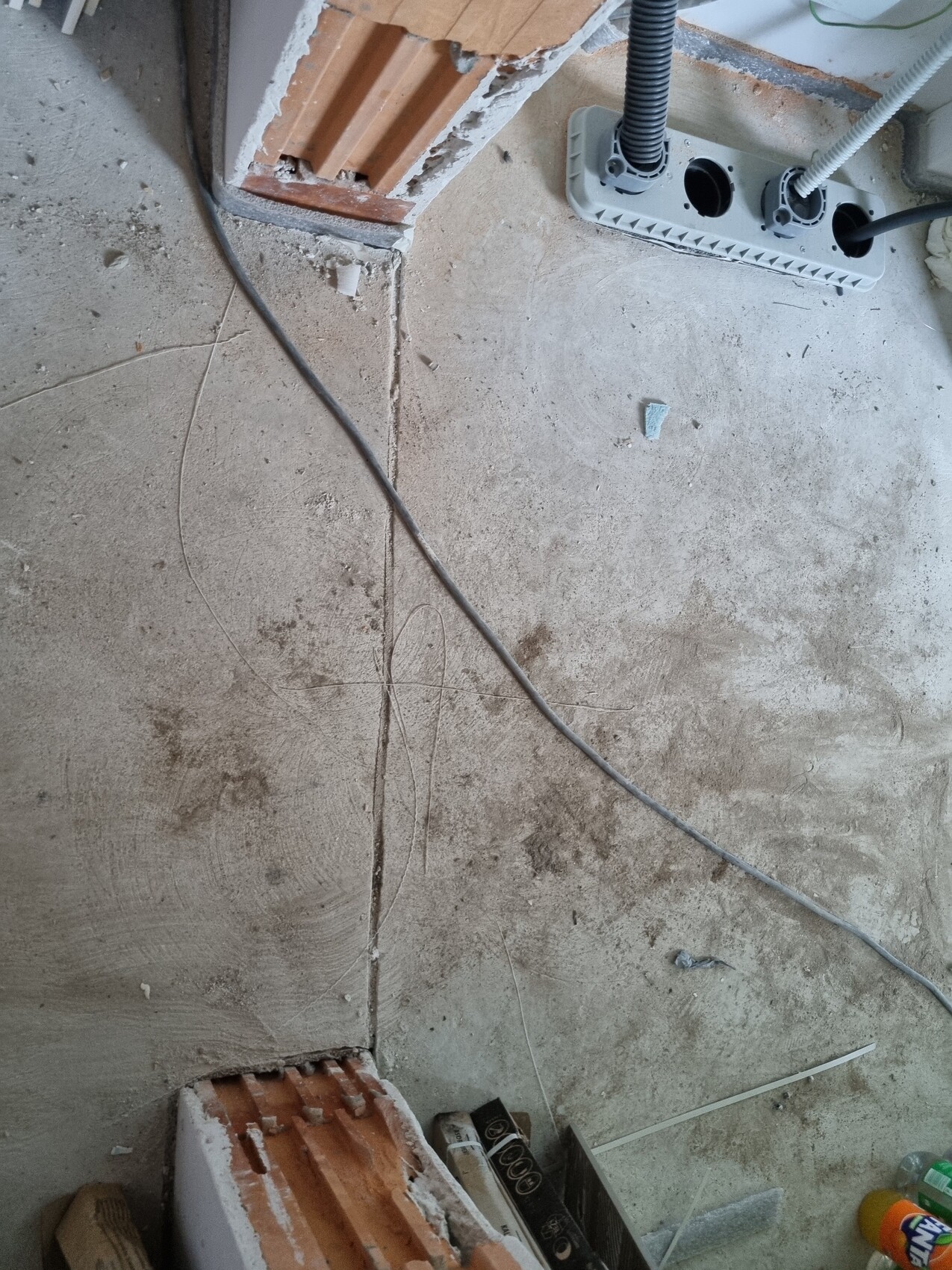Baustellenboden mit freiliegenden Kabeln, Mehrfachsteckerleiste und Ziegelresten.